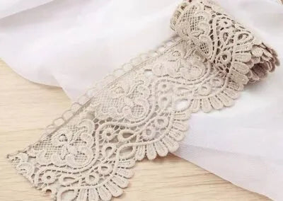 Pizzo guipure beige con motivi floreali e bordo smerlato su tessuto bianco