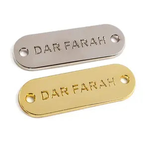 Zwei Metallplatten mit geprägtem Logo und Nählöchern – Silber und Gold