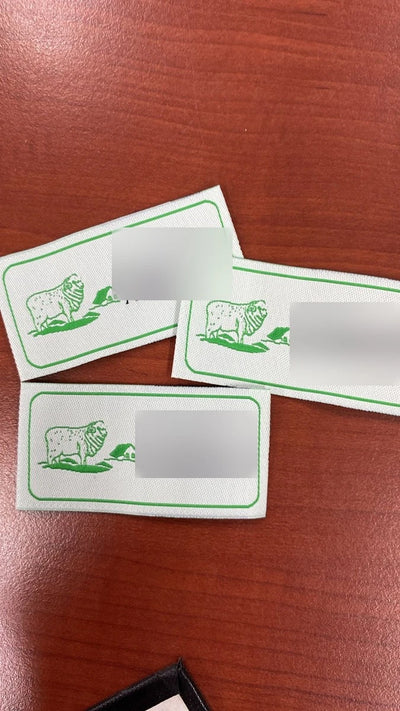 Etichette tessute con logo verde e nero su fondo bianco con cornice verde – set con cartellino