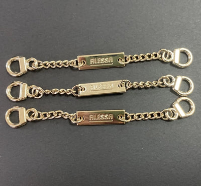 Zlatni lančić-vješalica s metalnom pločicom s logom i karikama za prišivanje na haljinu – primjer